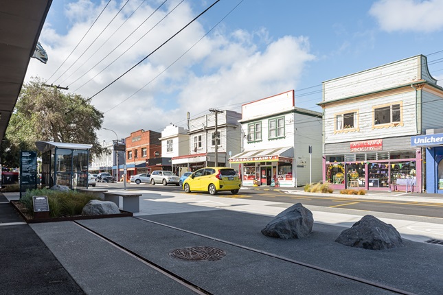 Urban streetscape with a close up of tram lines in the ground and shops in the background.