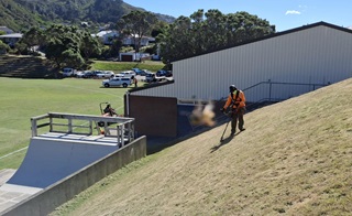 Man wearing high vis mowing on the side of a hill with a skate ramp at the bottom.