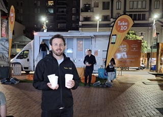 A man holding two cups outside of a caravan on Courtenay Place.