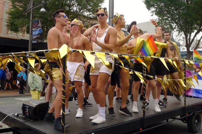 Pride Parade float with group of young men waving to crowds.