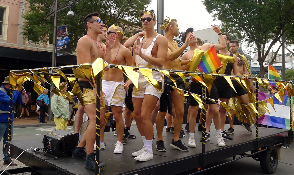 Pride Parade float with group of young men waving to crowds.