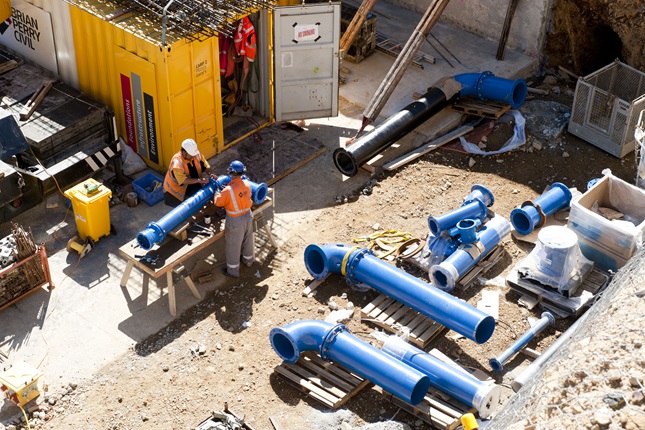 Two people in high vis working over a set of pipes.