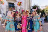 Five woman in colourful dresses infront a white building. 