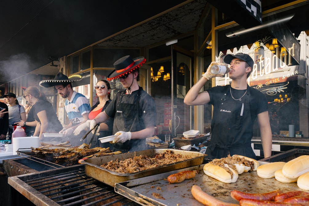People cooking outdoors infront of a restaurant.