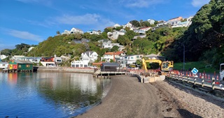 A sandy beach with a pathway running alongside it and houses in the background.
