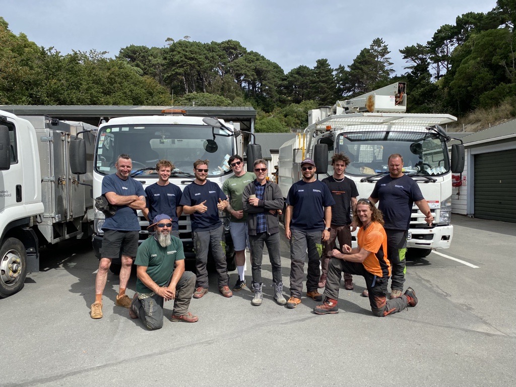 Group of men all standing together infront of trucks.