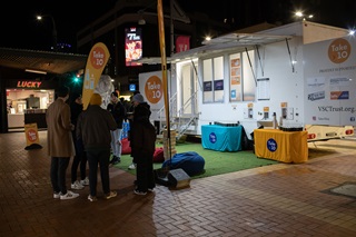 Group of people standing outside a caravan with Take 10 signage around them.