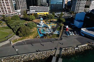 Birds eye view of penguin an area on the waterfront that is being used to create new penguin habitats, with a walkway, playground and buildings in the background.
