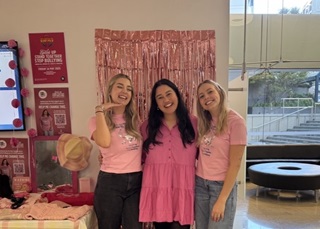 Three women standing together infront of a pink wall.