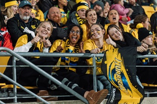 Group of hurricanes fans smiling in the stands wearing hurricanes merchandise.