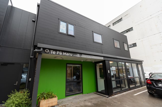 Exterior view of the Te Pā Maru building, a service provided by the Wellington City Mission, with a bright green entrance wall, large windows, and a black car parked outside.