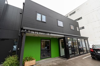 Exterior view of the Te Pā Maru building, a service provided by the Wellington City Mission, with a bright green entrance wall, large windows, and a black car parked outside.