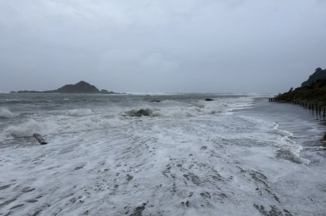 Dramatic weather along coast in Island Bay with big waves and island in background.