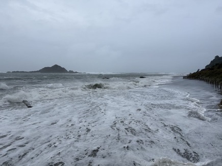 Dramatic weather along coast in Island Bay with big waves and island in background.