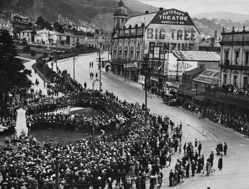 An archival photo of a temporary cenotaph in the city with crowds of people infront.