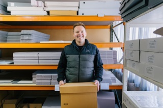 A person wearing a puffer jacket and smiling holding up a 'London box' for the archives.