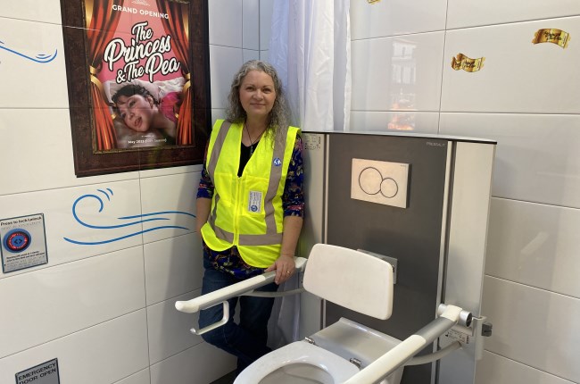 A woman in high vis standing between a wall and a toilet.