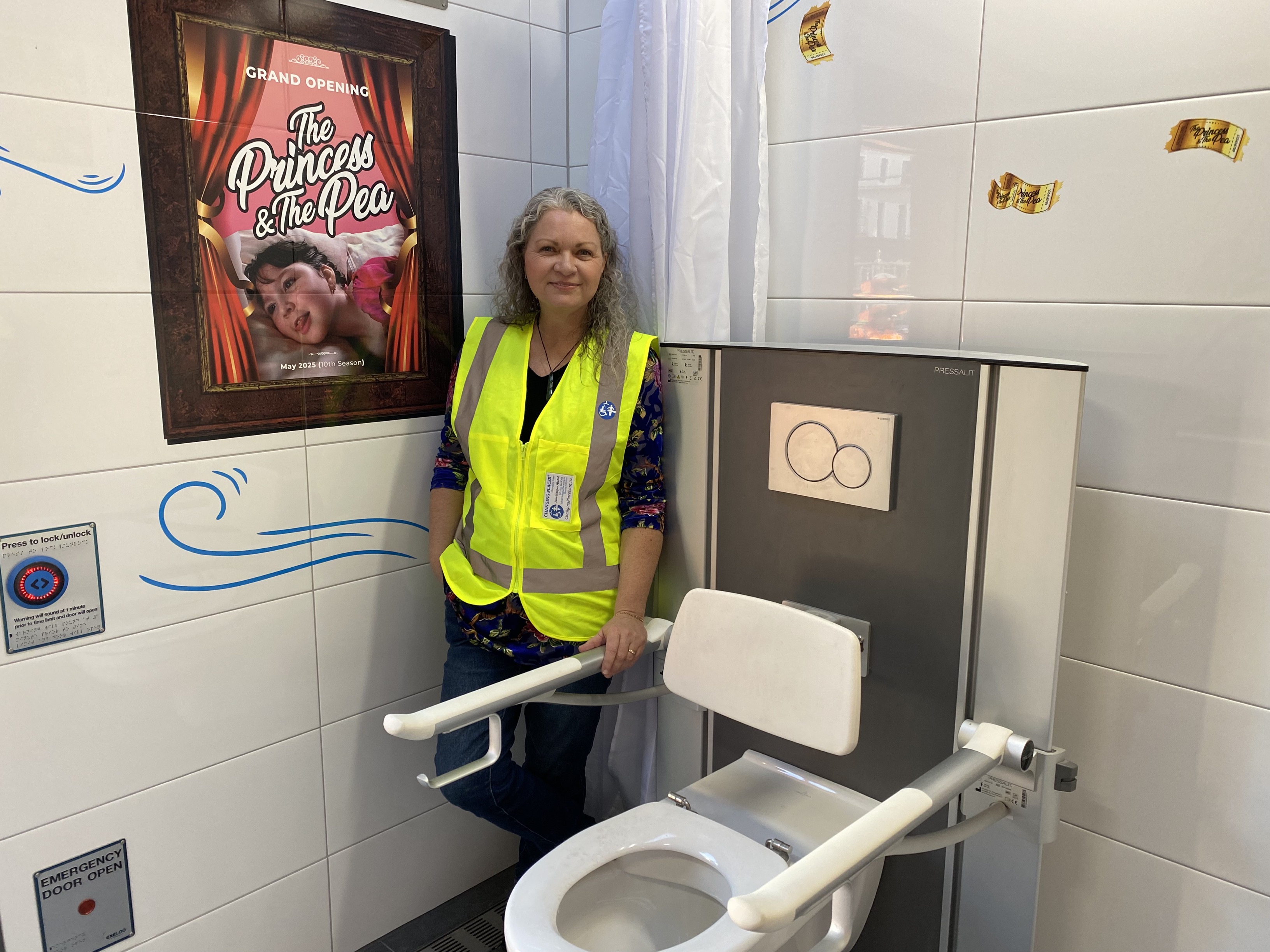 A woman in high vis standing between a wall and a toilet.