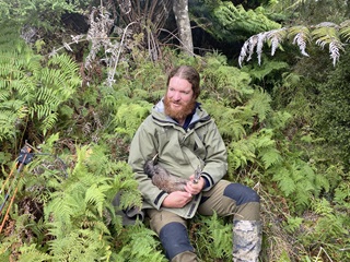A man in a green jacket holding a kiwi in a bush.