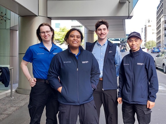 Group of four people standing on the street wearing blue uniform.