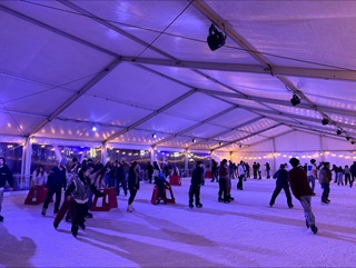 A bunch of people skating on an ice rink with purple and blue lights.