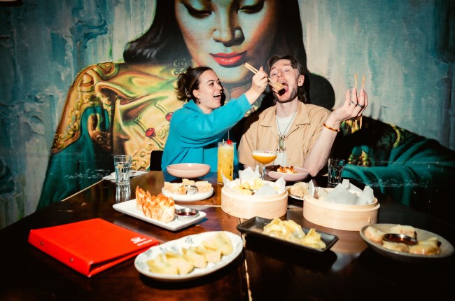 Couple eat with chop sticks at Chow with large Asian themed mural behind them.