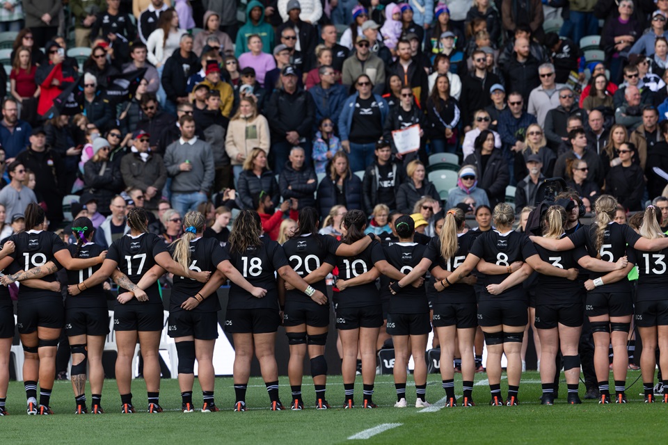 Black Ferns face the crowd from the field with arms linked ahead of match.