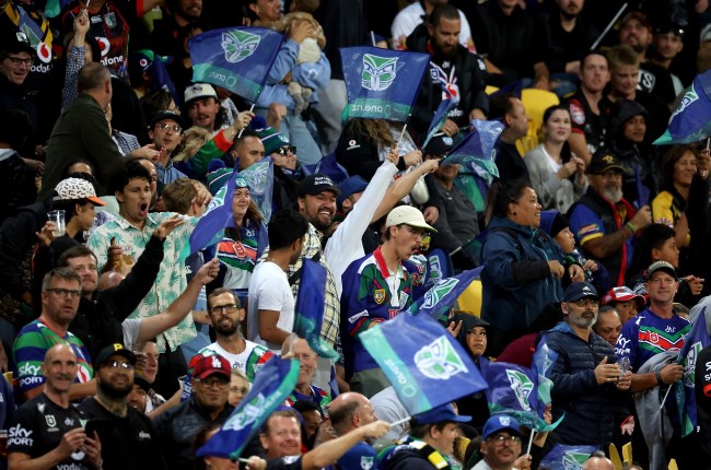 Fans in stands supporting Warriors game with flags and branded clothing.
