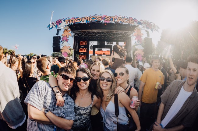 High Tide concert goers at festival in sun with stage in background.