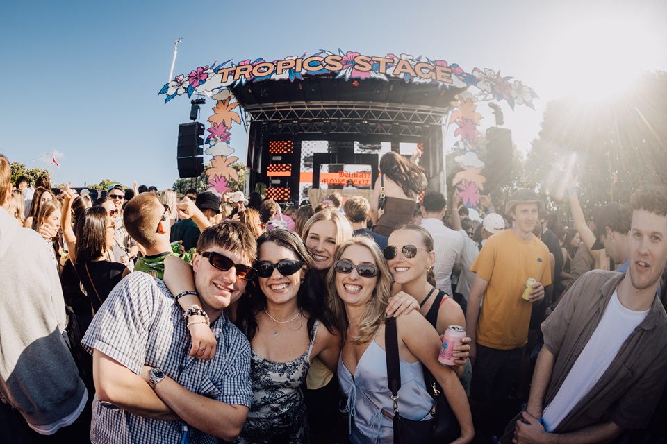 High Tide concert goers at festival in sun with stage in background.
