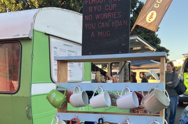 Mug.Cycle at Harbourside market with cups in forefront and signs and caravan in the background.