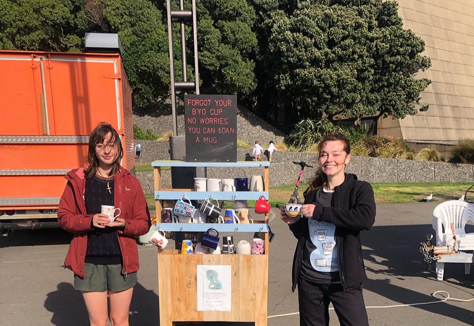Mug.Cycle team at Harbourside market with cups in forefront and signs in the background.