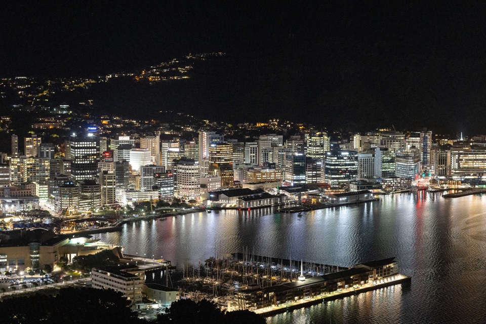 Wellington city buildings lit up at night, with their colourful reflections on the harbour.