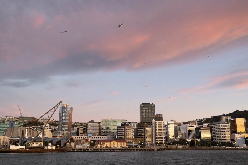 A dusky pink and blue sky above a cityscape that stretches around a harbour.