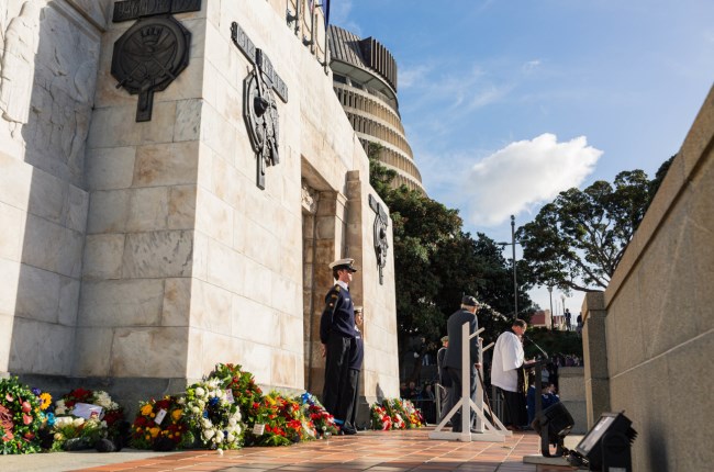 Soldiers stand beside a memorial surrounded by wreaths at an Anzac Day service.
