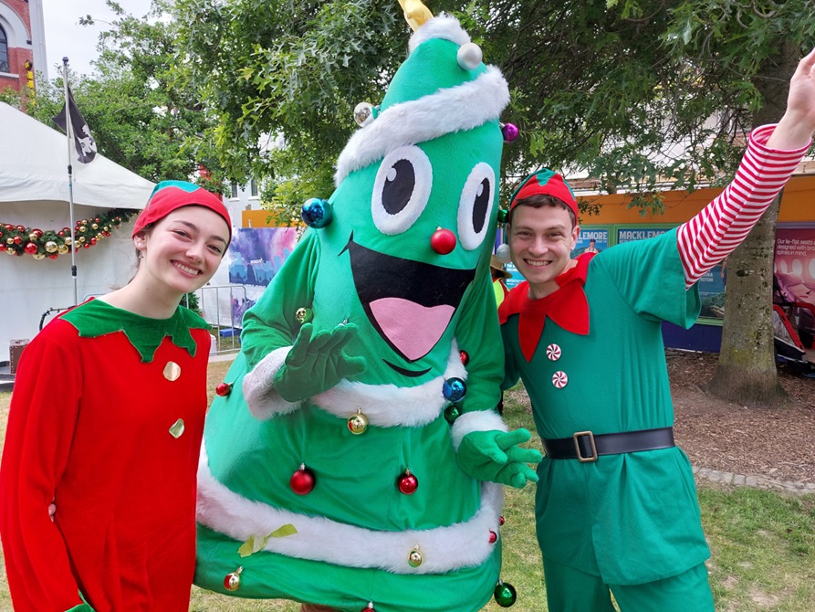 People dressed as Christmas elves pose with a person dressed as a Christmas tree.