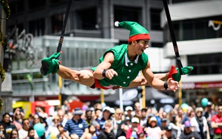 A aerialist circus performer dressed in a red and green elf costume performs in front of an audience.
