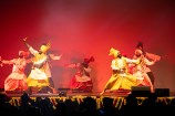 Five dancers perform on stage in front of a silhouetted crowd.