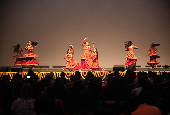 Seven women dancing on a stage. Four are twirling causing their dresses to billow.