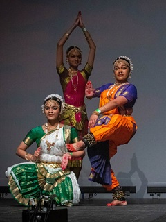 Three dancers on stage in traditional brightly-coloured dress.