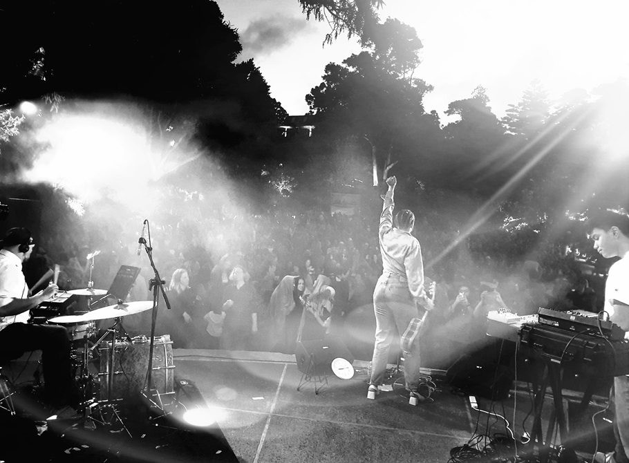 An artist standing on stage with a large crowd at Botanic Gardens soundshell.