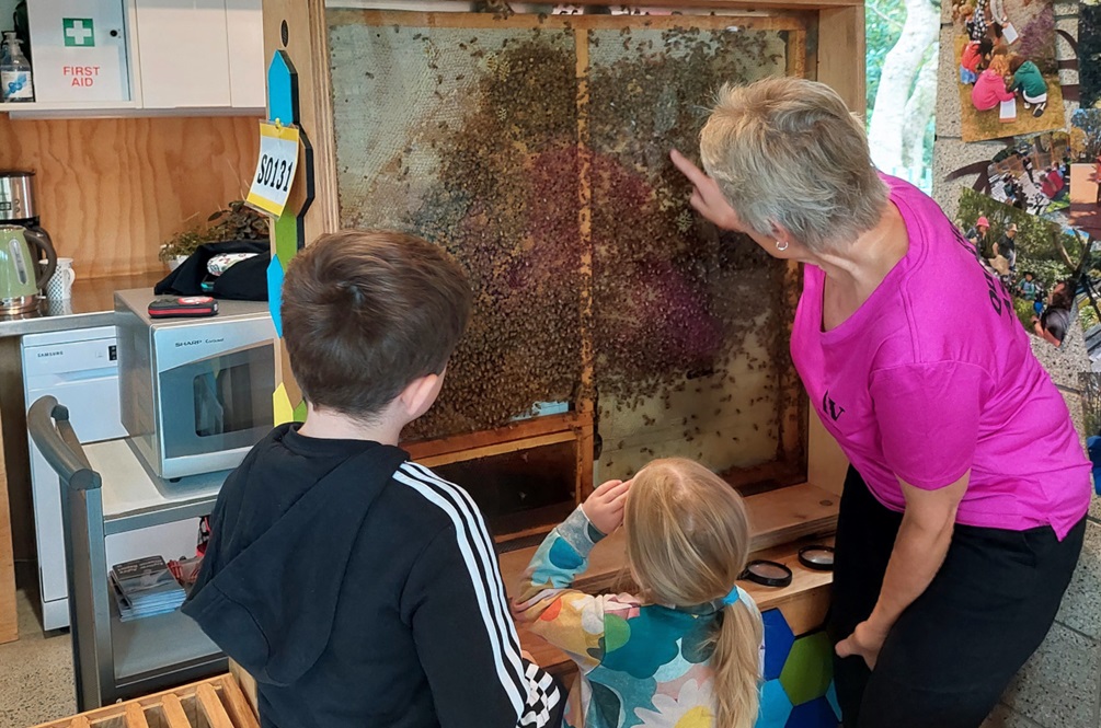 A woman shows two children a display of live bees.