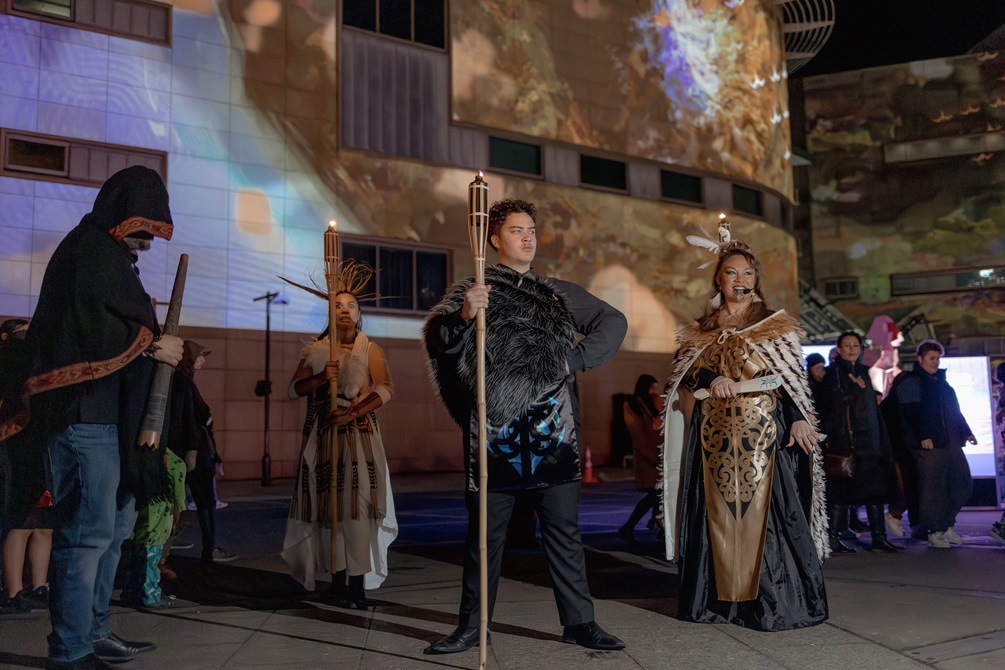 A group of costumed performers pose in front of Te Papa museum.