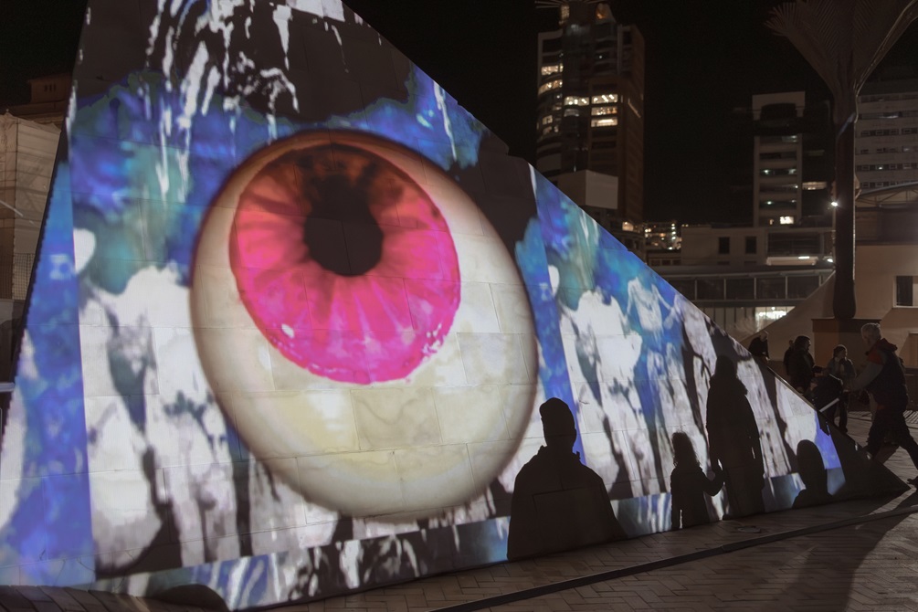 A stylised eyeball projected onto a sculptural pyramid in Civic Square as part of a multimedia display.