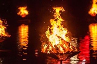 Burning braziers floating in water at night.