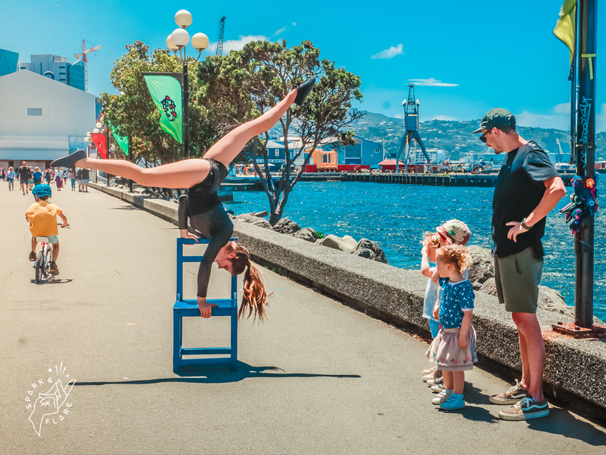 A performer on the waterfront doing a handstand on a chair and the splits in the air.