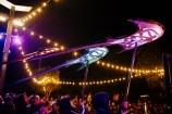 Purple and blue kites shaped like stingrays are carried above the crowd.