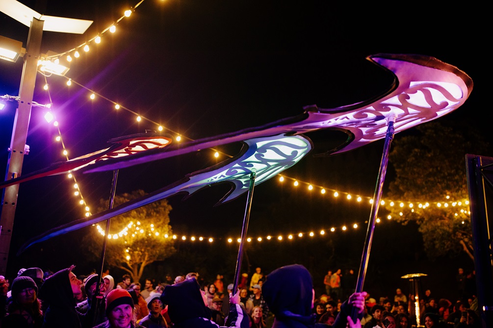 Purple and blue kites shaped like stingrays are carried above the crowd.