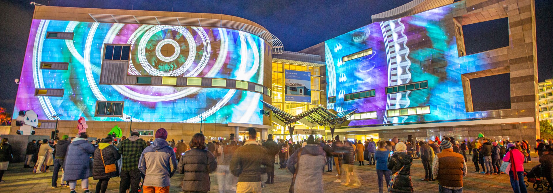 A crowd of onlookers watching an audiovisual display projected on the exterior walls of Te Papa during a past Matariki event.