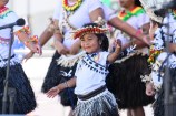 A child in traditional dress performs as part of a troupe with other performers in the background.